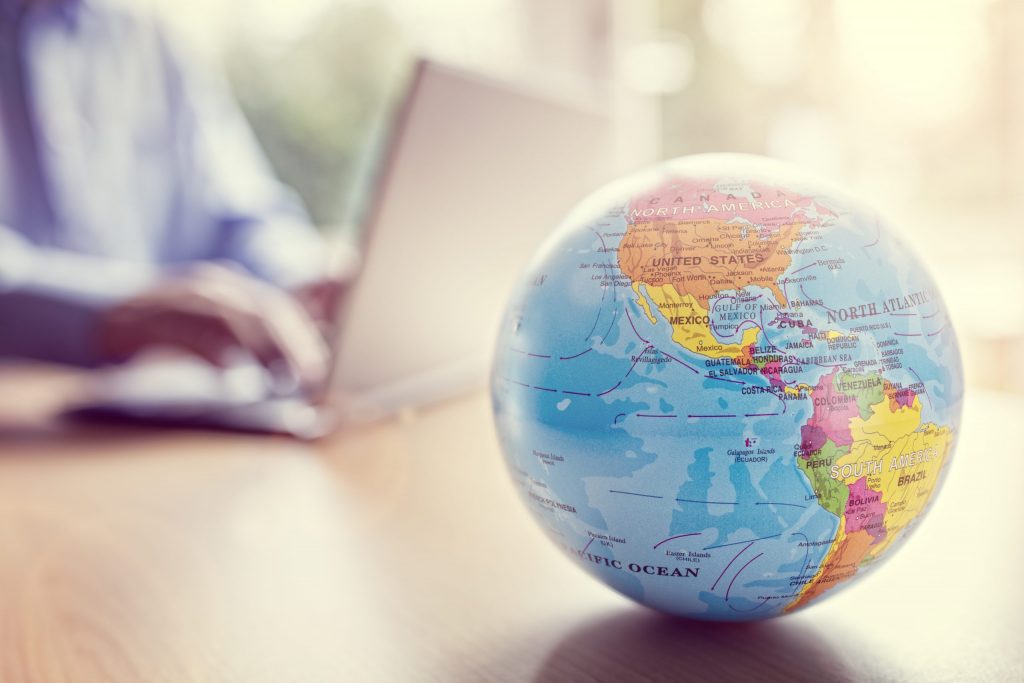 Close-up of a globe with a person working on a laptop in the background, symbolising Mocean SMS Messaging Campaign solutions empowering Malaysian businesses globally.