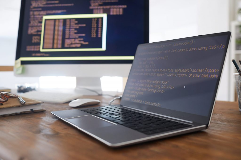 Laptop and desktop with code on screens, representing Mocean SMS API integration for developers in Malaysia.